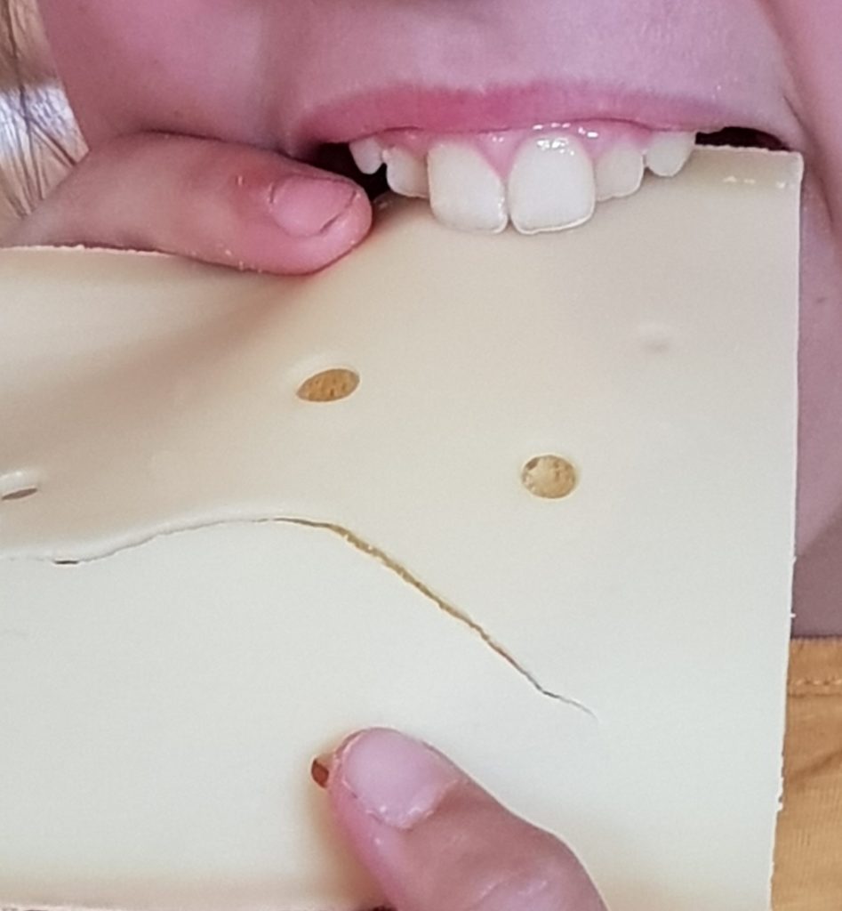 Ein Kind beißt in eine Käsescheibe, die wie ein Gesicht aussieht