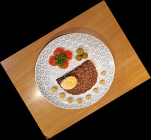 Auf einem gemusterten Teller befinden sich eine Scheibe Vollkornbrot, Tomaten, Oliven und Maiskölbchen