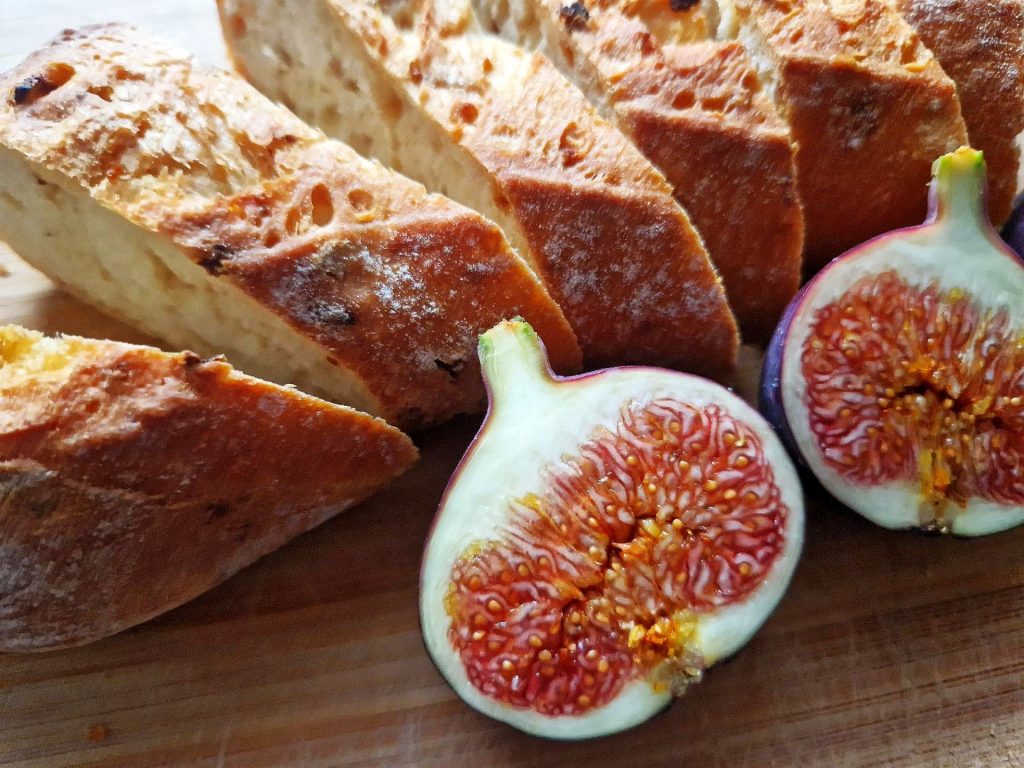 eine mittig aufgeschnittene Feige liegt vor aufgeschnittenem Brot
