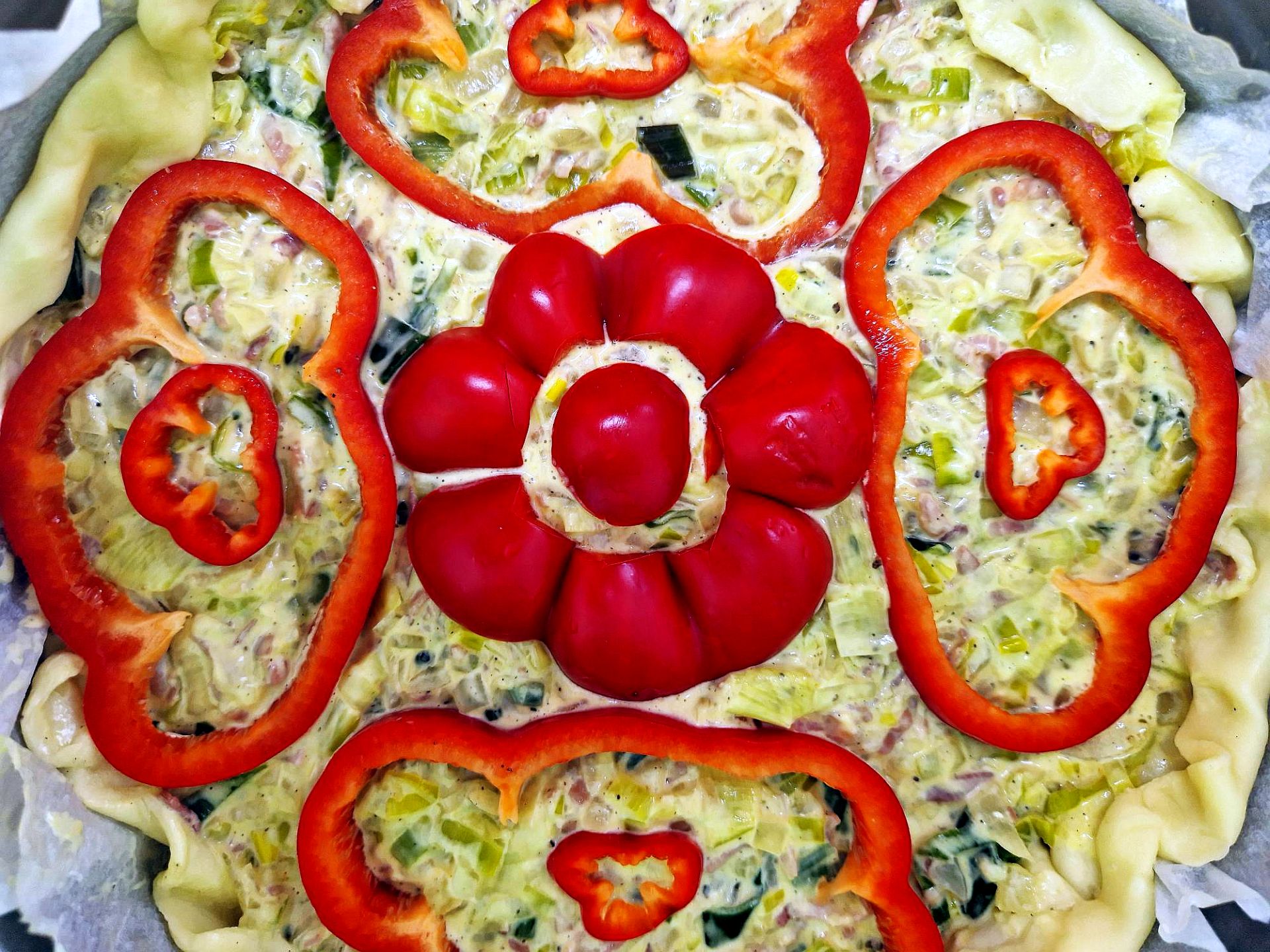Lauchkuchen ungebacken, verziert mit Paprikaringen